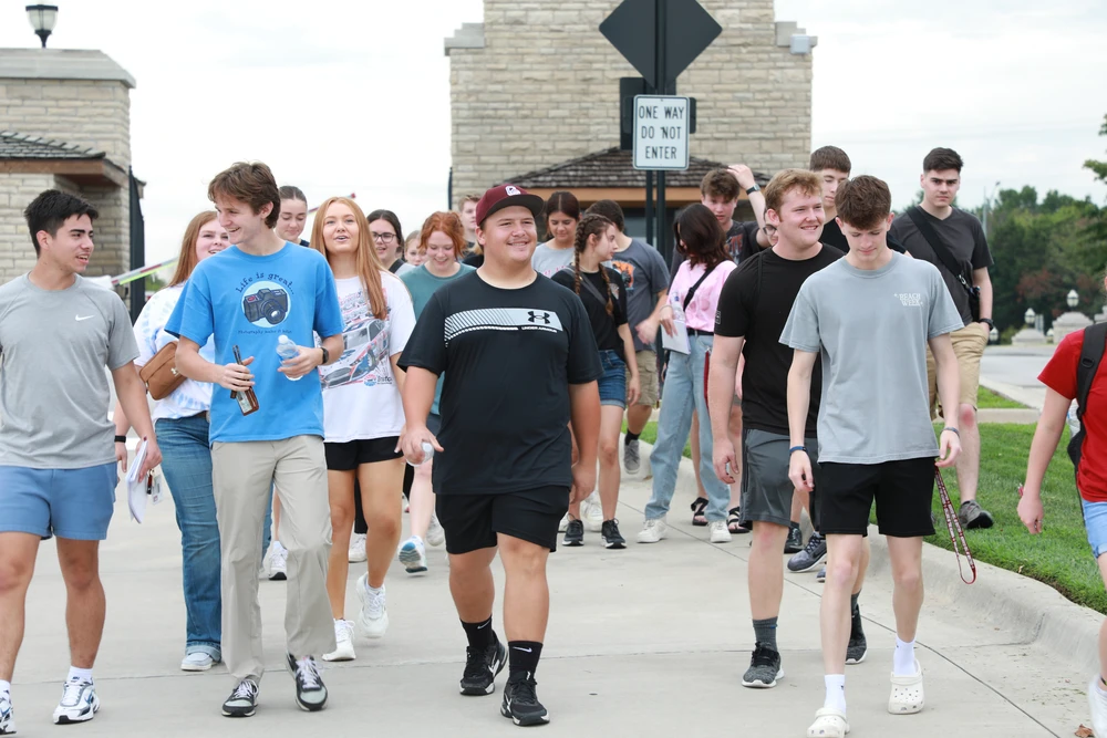 Young men and women walking on road together in front of a gate.